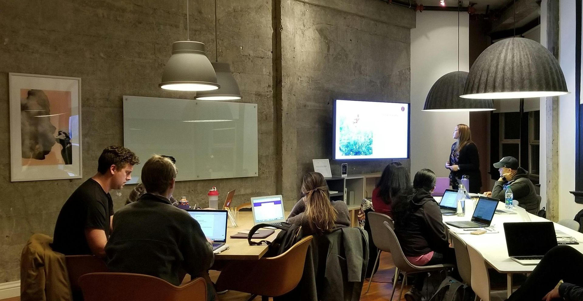 Diverse team collaborating in a modern office setting with laptops and presentation screen.